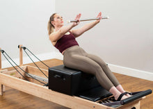 Load image into Gallery viewer, Pilates professional exercising on a Studio Reformer and box with bar from the traditional accessory kit