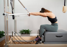Load image into Gallery viewer, Woman utilizing reformer and trapeze for strength and flexibility training | caption::Shown in Storm Upholstery