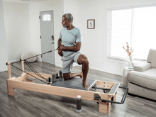 Load image into Gallery viewer, Man engaged in a Pilates exercise using a Studio Reformer with a XSR footbar with a Revo Springbar, emphasizing proper alignment and form.
