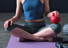 Load image into Gallery viewer, Woman holding a red playground ball for Pilates.