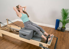 Load image into Gallery viewer, Close-up of the Contour Sitting Box being used by a woman during a Pilates session.

