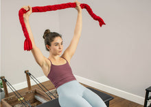 Load image into Gallery viewer, A woman gripping a red towel designed for Pilates strength and stability exercises.