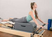 Load image into Gallery viewer, A woman leveraging a contour sitting box for enhanced stability while on a reformer.