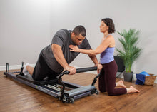 Load image into Gallery viewer, Female instructor guiding a man on how to use an Allegro Stretch Pilates Reformer.