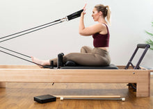 Load image into Gallery viewer, Pilates professional exercising on a Studio Reformer with the traditional accessory kit

