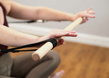 Load image into Gallery viewer, Close up of a Pilates professional exercising on a Studio Reformer with bar from the traditional accessory kit
