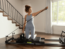 Load image into Gallery viewer, Woman performing an exercise on a Metro-IQ Pilates Reformer, focusing on her posture and alignment.

