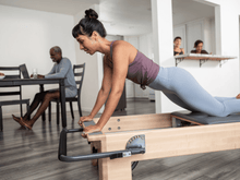 Load image into Gallery viewer, Woman demonstrating a controlled Pilates movement on a Pilates Studio Reformer, highlighting her core stability and precise alignment.
