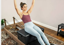Load image into Gallery viewer, Woman seated on New York-style Pilates reformer box.
