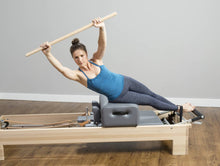 Load image into Gallery viewer, Woman using a maple dowel on a reformer with a sitting box.
