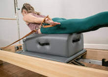 Load image into Gallery viewer, Woman exercising on a CenterLine Sitting Box on a reformer.
