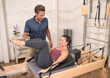 Load image into Gallery viewer, Instructor guiding woman on using Pilates wedge for back support on a reformer.
