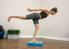 Load image into Gallery viewer, Woman performing a one-leg stand on a blue Balance Pad.
