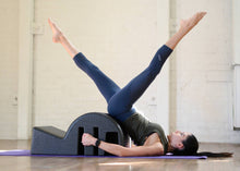 Load image into Gallery viewer, A woman performing the windmill exercise on a Clara-Step Pilates Barrel Lite.
