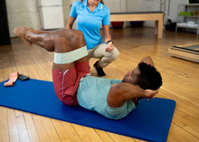 Load image into Gallery viewer, A man stretching his arms and torso using a resistance band on a blue exercise mat.

