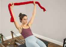 Load image into Gallery viewer, A woman gripping a red towel designed for Pilates strength and stability exercises.
