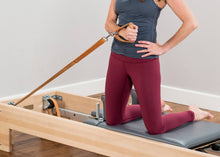 Load image into Gallery viewer, A woman utilizing a leather and wood handle during her workout on a Pilates reformer.
