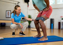 Load image into Gallery viewer, A man stretching his torso using a durable resistance band on a blue mat.
