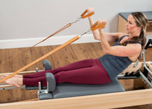 Load image into Gallery viewer, Woman pulling leather straps attached to an Allegro Reformer.
